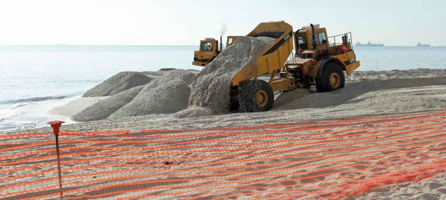 trucks dumping sand on eroding coastline